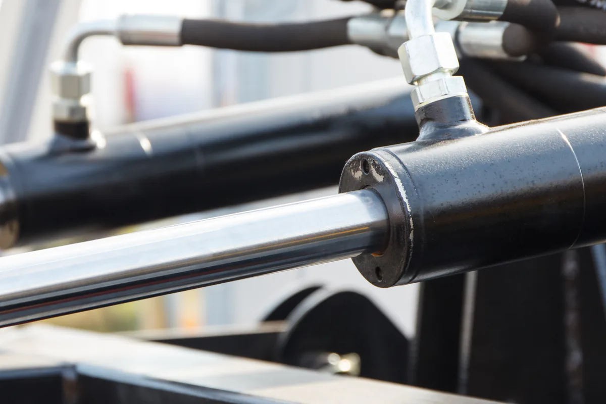 Närbild på ett hydraulsystem med cylinder, kolvstång och slangar